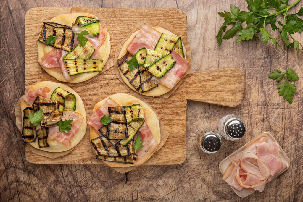 Tagliere con pizzette con mozzarella, pancetta e verdure grigliate